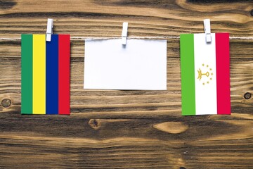 Hanging flags of Mauritius and Tajikistan attached to rope with clothes pins with copy space on white note paper on wooden background.Diplomatic relations between countries.