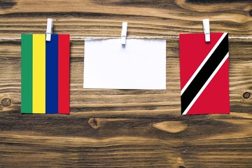 Hanging flags of Mauritius and Trinidad And Tobago attached to rope with clothes pins with copy space on white note paper on wooden background.Diplomatic relations between countries.