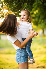 Portrait of beautiful mother with love hugging her daughter in bright yellow sunlight in the park....