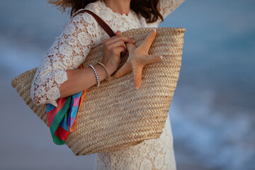 Closeup on stylish woman holding beach straw bag and starfish
