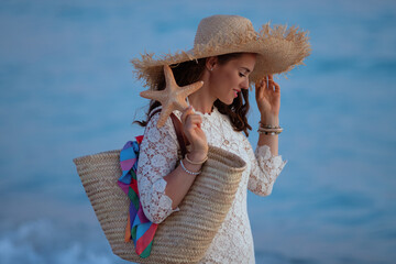woman on beach at sunset holding beach straw bag and starfish