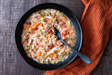 Puerto Rican Chicken Rice Soup in a black stoneware bowl on a dark wood table, black metal spoon, orange cloth napkin