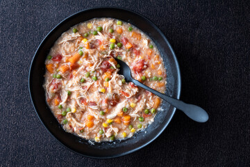 Puerto Rican Chicken Rice Soup in a black stoneware bowl on a dark tablecloth, black metal spoon