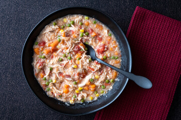 Puerto Rican Chicken Rice Soup in a black stoneware bowl on a dark tablecloth, black metal spoon, maroon cloth napkin