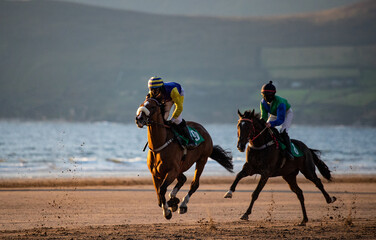 Two race hoses and jockeys racing on the beach at sunset, horse racing on the west coast of Ireland
