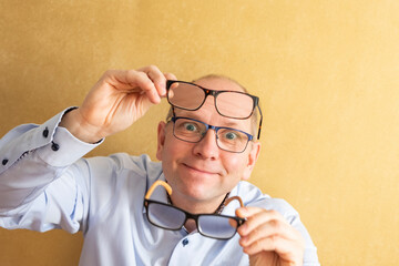 A man chooses and tries on glasses for sight. White man in a blue shirt on a background of a yellow...
