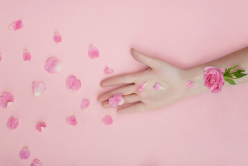 Hand with pink flowers and petals lying on a paper background. Cosmetics for hand skin care. Natural petal cosmetics, essential oils, anti-wrinkle and anti-aging hand care