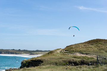 paraglider flying above a picturesque sandy beach on te rocky coast of Brittany