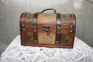 Closed dusty beautiful brown chest on a white knitted tablecloth against the concrete gray streaked wall.