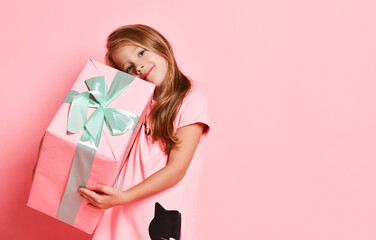 Christmas and New Year. Blonde kid girl in pink dress holding a big present gifts box, hugging, has got best on pink