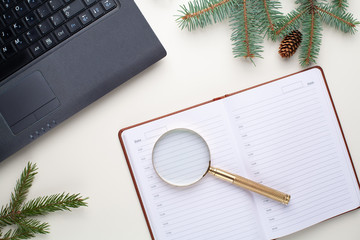 The laptop lies on a white table with a planner and a magnifier with a branch of spruce