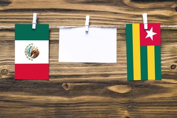 Hanging flags of Mexico and Togo attached to rope with clothes pins with copy space on white note paper on wooden background.Diplomatic relations between countries.