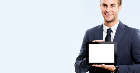 Happy smiling businessman showing blank noname tablet pc monitor, isolated over grey background, with copy space area for some slogan or text. Success in business concept picture.