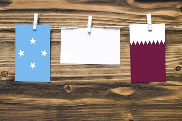 Hanging flags of Micronesia and Qatar attached to rope with clothes pins with copy space on white...
