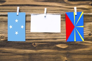 Hanging flags of Micronesia and Reunion attached to rope with clothes pins with copy space on white note paper on wooden background.Diplomatic relations between countries.