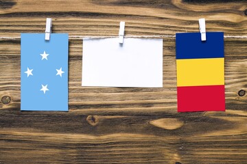 Hanging flags of Micronesia and Romania attached to rope with clothes pins with copy space on white note paper on wooden background.Diplomatic relations between countries.