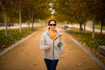 Mujer con gafas de sol corriendo en un parque en otoño