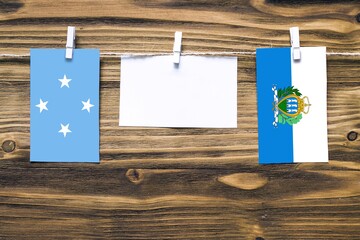 Hanging flags of Micronesia and San Marino attached to rope with clothes pins with copy space on...