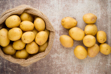 Sack of fresh raw potatoes on wooden background, top view.