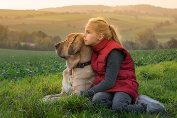 Beste Freunde - Ein Kind sitzt mit seinem Hund, einem Broholmer, auf einem Feldweg, umarmt ihn und...