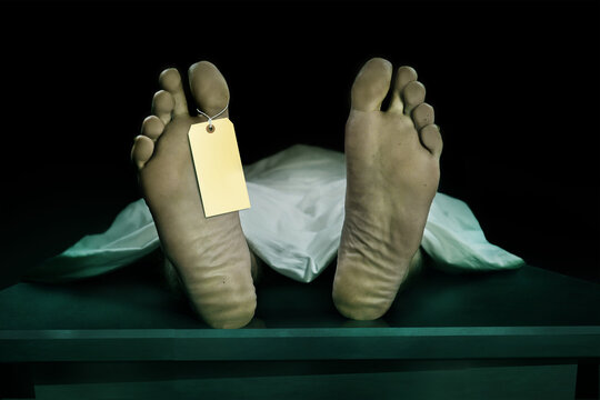 Male human body lying dead at morgue with blank identity label and covered with sheet . Close-up foot of man cadaver with identification toe tag in death concept