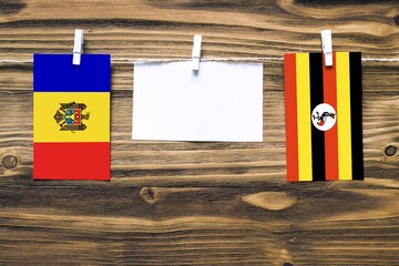 Hanging flags of Moldova and Uganda attached to rope with clothes pins with copy space on white note paper on wooden background.Diplomatic relations between countries.