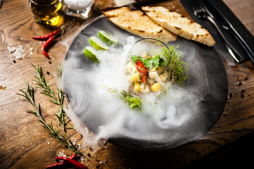Scallop ceviche served in black bowl with liquid ice smoke