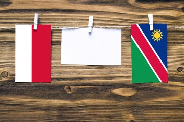 Hanging flags of Monaco and Namibia attached to rope with clothes pins with copy space on white note paper on wooden background.Diplomatic relations between countries.