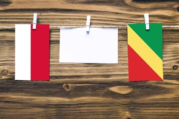 Hanging flags of Monaco and Republic Of The Congo attached to rope with clothes pins with copy space on white note paper on wooden background.Diplomatic relations between countries.