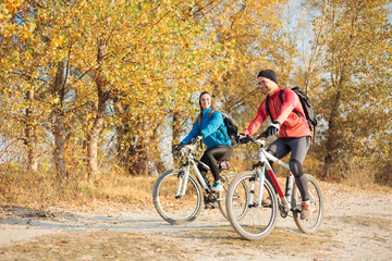 Smiling young couple enjoying relaxing mountain bike ride through the forest on a beautiful cold autumn morning. Active and healthy lifestyle