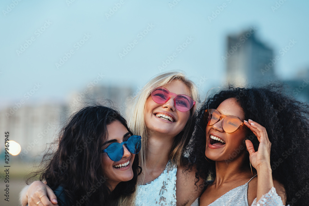 Wall mural three beautiful women with colorful sunglasses standing at evening outdoors