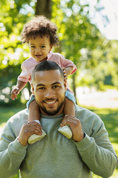 Young father carrying son on shoulders outdoors. Portrait of a young dad and his child in the park.