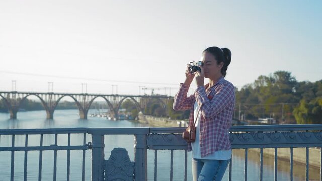 Beautiful Woman Taking pictures on a Film Camera Standing on the Bridge