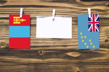 Hanging flags of Mongolia and Tuvalu attached to rope with clothes pins with copy space on white note paper on wooden background.Diplomatic relations between countries.