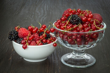 Composition of berries (red currants, blueberries, blackberries, raspberries), fruit in a bowl on a dark brown table.