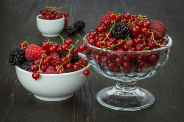 Composition of berries (red currants, blueberries, blackberries, raspberries), fruit in a bowl on a dark brown table.