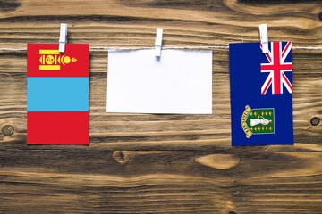 Hanging flags of Mongolia and British Virgin Islands attached to rope with clothes pins with copy space on white note paper on wooden background.Diplomatic relations between countries.