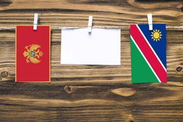 Hanging flags of Montenegro and Namibia attached to rope with clothes pins with copy space on white note paper on wooden background.Diplomatic relations between countries.