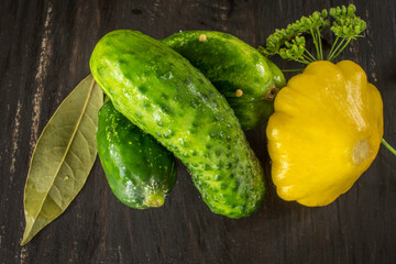 Composition of ground cucumbers, cymling with a sprig of garden dill, bay leaf on a dark brown table.