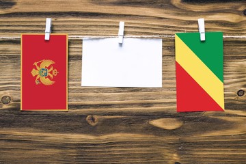 Hanging flags of Montenegro and Republic Of The Congo attached to rope with clothes pins with copy space on white note paper on wooden background.Diplomatic relations between countries.