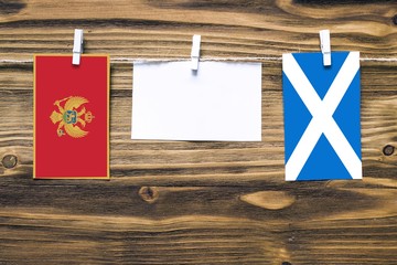 Hanging flags of Montenegro and Scotland attached to rope with clothes pins with copy space on white note paper on wooden background.Diplomatic relations between countries.