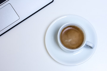vista superior taza de café cremoso sobre mesa blanca de oficina con ordenador portátil