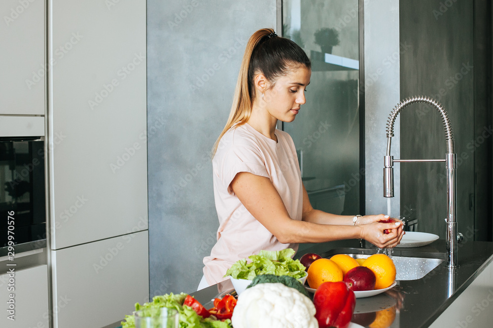 Wall mural young woman washes vegetables in the kitchen