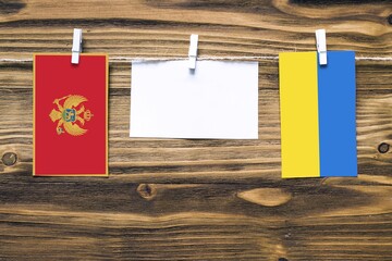 Hanging flags of Montenegro and Ukraine attached to rope with clothes pins with copy space on white note paper on wooden background.Diplomatic relations between countries.