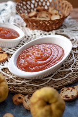 Homemade jelly quince in a white crockery containers with some quince fruits and little toasts to spread.