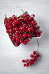 Spilled red currants in a white container on a white table, shallow depth of field