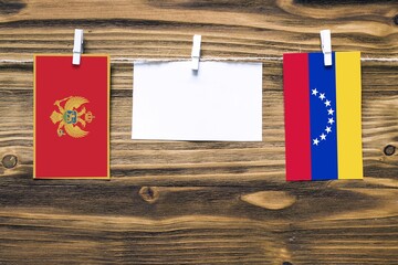 Hanging flags of Montenegro and Venezuela attached to rope with clothes pins with copy space on white note paper on wooden background.Diplomatic relations between countries.