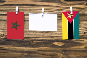 Hanging flags of Morocco and Mozambique attached to rope with clothes pins with copy space on white note paper on wooden background.Diplomatic relations between countries.