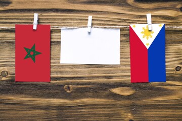 Hanging flags of Morocco and Philippines attached to rope with clothes pins with copy space on white note paper on wooden background.Diplomatic relations between countries.