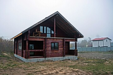 large brown unfinished wooden house in dry grass in the yard